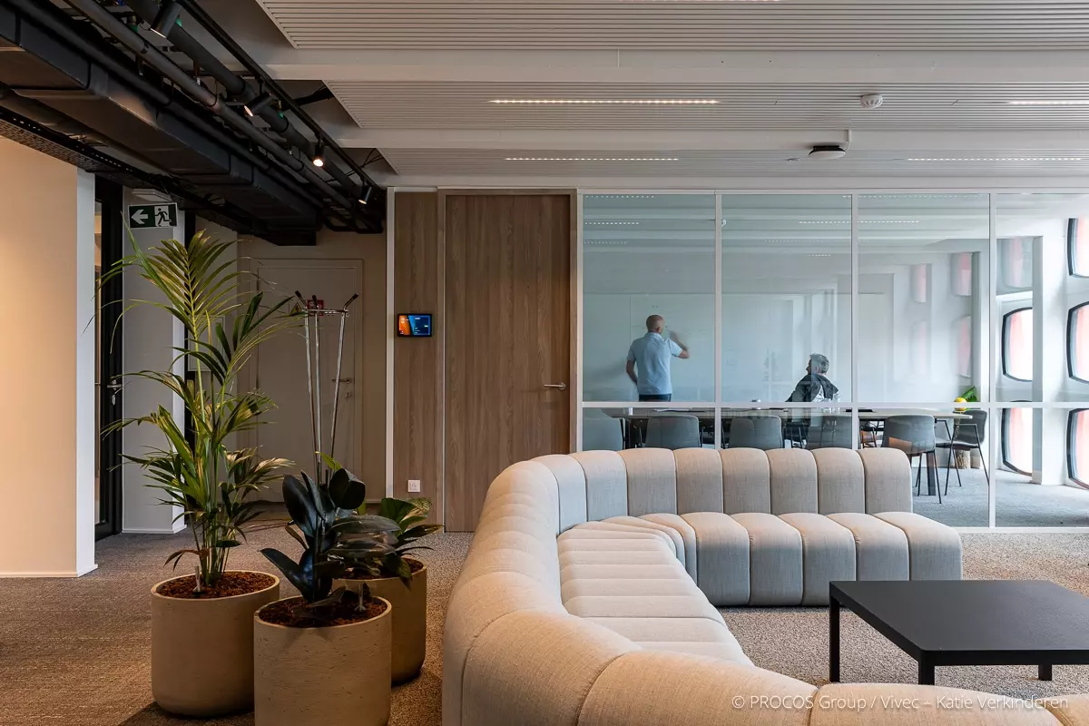 Bureau moderne avec canapé incurvé, plantes et salle de réunion en verre. 