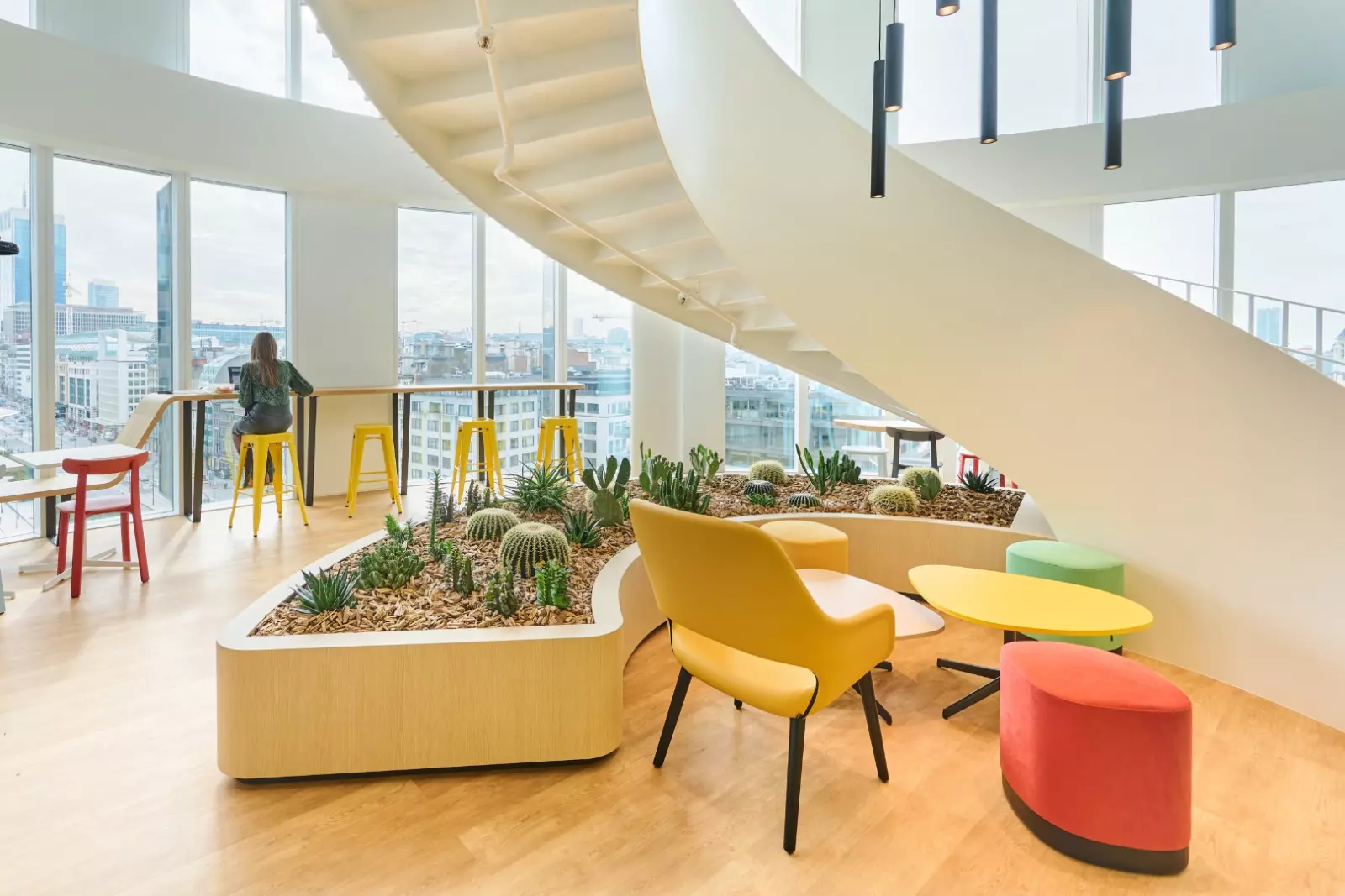Intérieur de bureau moderne avec mobilier coloré, jardin intérieur central avec des cactus et grandes fenêtres.