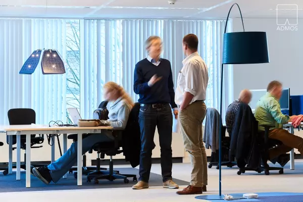Modern office with employees working and talking, blue designer lamps and white desks.