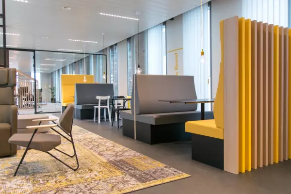 Modern office with yellow and grey privacy booths, industrial pendant lights, and a patterned rug.